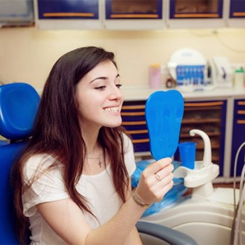 young woman seeing her new smile in a mirror after dental bonding    